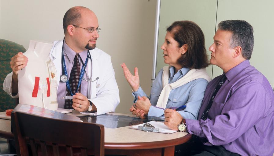 doktor a dva pacienti, muž a žena, sedí za stolem a povídají si